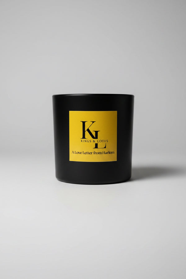 A black candle jar with a large yellow label reading 'KINGS & LOTUS' and 'A Love Letter from Harlem', 