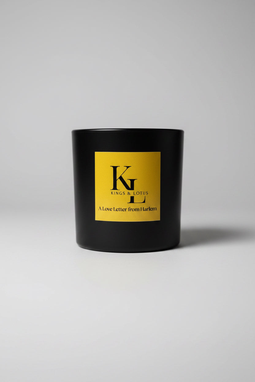 A black candle jar with a large yellow label reading 'KINGS & LOTUS' and 'A Love Letter from Harlem', 