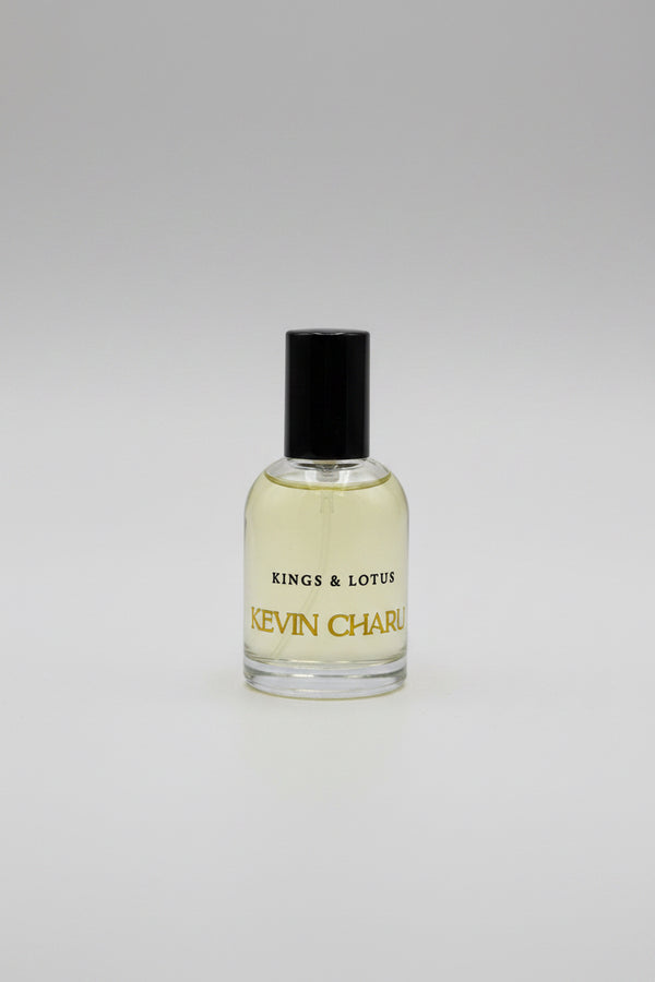 A bottle of Kevin Charles Kings & Lotus cologne with a black cap and gold lettering, resting on a black velvet surface with its black packaging box in the background.