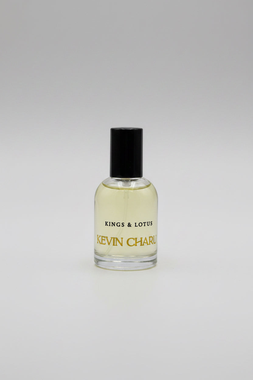 A bottle of Kevin Charles Kings & Lotus cologne with a black cap and gold lettering, resting on a black velvet surface with its black packaging box in the background.