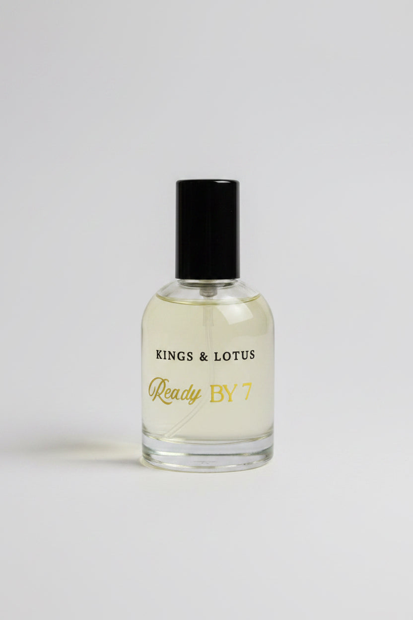 A bottle of Kings & Lotus Ready By 7 fragrance, featuring a clear glass bottle filled with light yellow liquid and a black cap, resting on a black surface with a branded black box in the background.