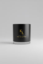A black glass jar candle with gold lettering reading 'Kings s + Lotus Take Care of Home'